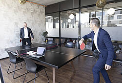 Zwei Männer im Anzug spielen in einem Büro Tischtennis.