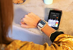 Eine Frau hält ihre Smartwatch an ein mobiles Bezahlterminal, um ihren Kaffee zu bezahlen.