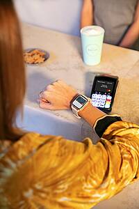 Eine Frau hält ihre Smartwatch an ein mobiles Bezahlterminal, um ihren Kaffee zu bezahlen.