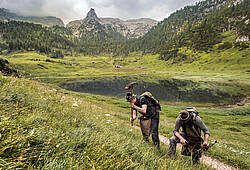 Zwei Helfer der Enzianbrennerei Grassl graben am Funtensee in den Berchtesgadener Alpen nach Enzianwurzeln. Im Hintergrund der Funtensee.