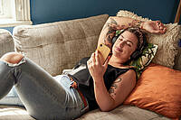 Eine junge Frau liegt auf einem Sofa und schaut in ihr Smartphone.