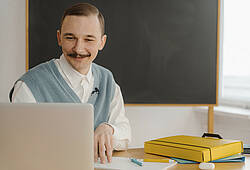 Ein Hipster mit Schnurrbart sitzt vor einem Laptop.