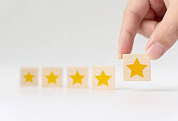 Ein Mensch ergänzt vier Holzplättchen mit je einem gelben Stern darauf um ein fünftes Holzplättchen (Symbolbild für Kundenzufriedenheit).