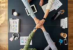 Vier Menschen legen in einem Büro die Hände übereinander (Symbolbild).
