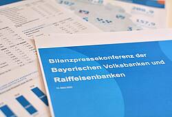 Unterlagen zur Jahresbilanz 2022 der bayerischen Volksbanken und Raiffeisenbanken liegen auf einem Tisch.