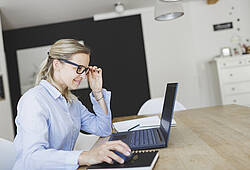 Eine Frau sitzt an einem Tisch und arbeitet an einem Laptop.