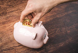 Eine Person steckt eine Bitcoin-Münze in ein Sparschwein (Symbolbild).