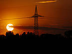 Ein Strommast zeichnet sich als Silhouette vor der untergehenden Sonne ab.