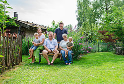 Eine Familie mit zwei Kindern und Großeltern sitzt im Garten auf einer Bank.