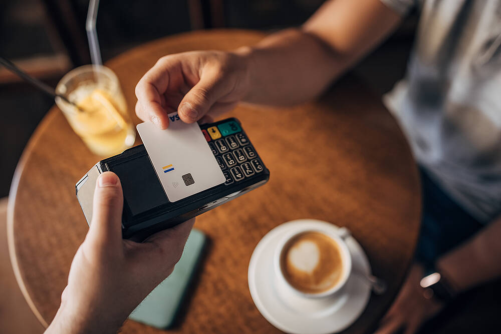Ein Mann bezahlt in einem Café seinen Cappuccino mit Karte.