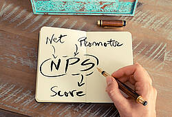 Eine Person schreibt in ein Notizbuch die Buchstaben NPS und Net Promoter Score. Zu sehen ist nur die Hand (Symbolbild).