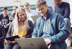 Junge Menschen sitzen im Freien und arbeiten mit Tablet und Laptop (Symbolfoto).