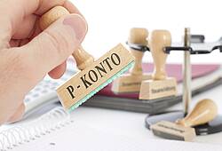 Eine Person nimmt einen Stempel mit der Aufschrift P-Konto aus einem Stempelhalter (Symbolfoto).