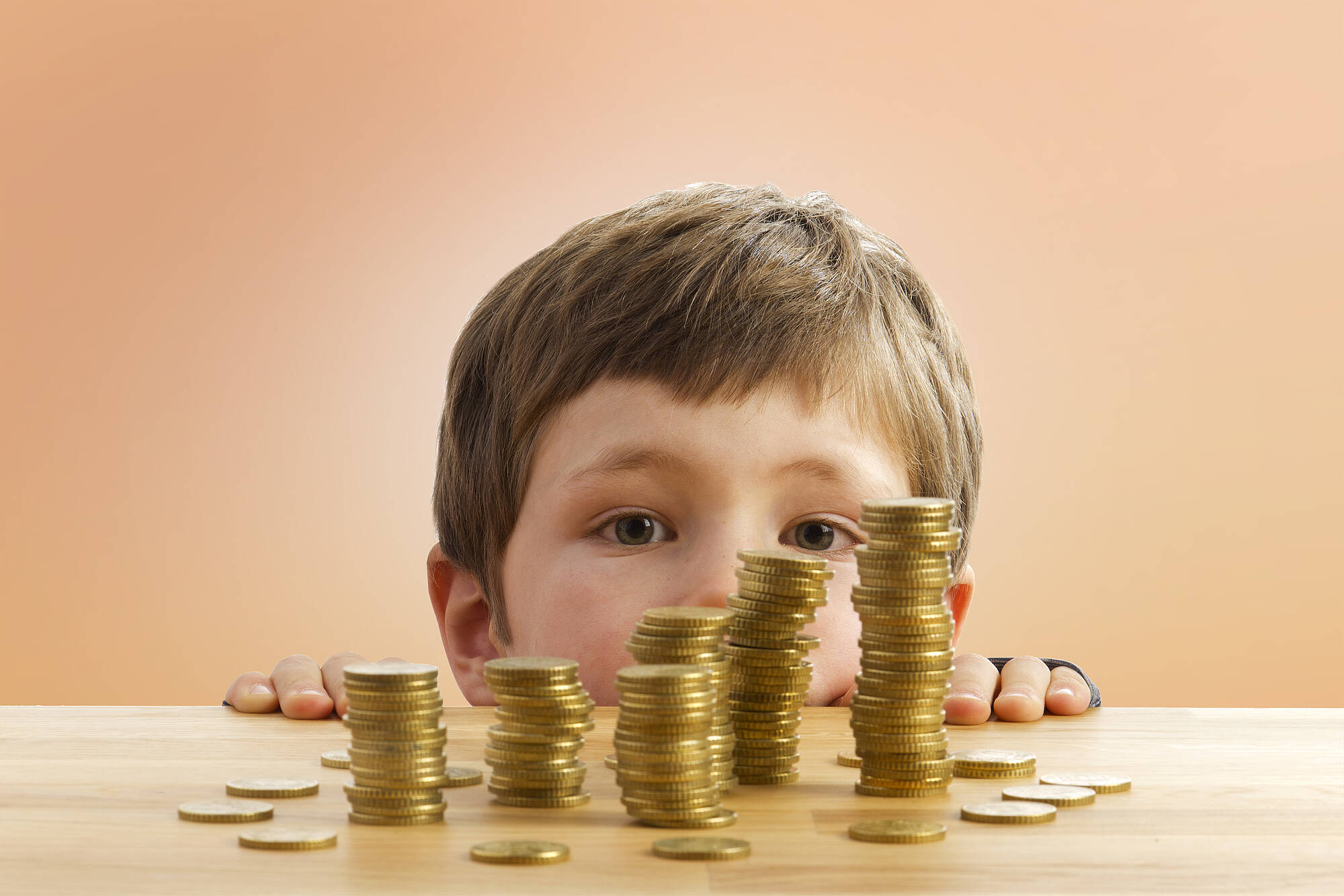 Ein kleiner Junge lugt über eine Tischkante auf mehrere Stapel 50-Cent-Münzen.