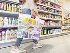 Eine Kundin läuft durch einen dm-Supermarkt. In der Hand hält sie eine Tüte mit dm-Logo.