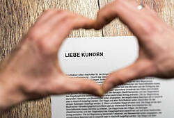 Zwei Hände formen ein Herz über einem Brief mit der Anrede „Liebe Kunden“ (Symbolbild).