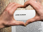 Zwei Hände formen ein Herz über einem Schreiben mit der Anrede „Liebe Kunden“ (Symbolbild).