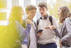 Jugendliche schauen auf ein Smartphone und diskutieren.
