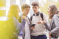 Jugendliche schauen auf ein Smartphone und diskutieren.