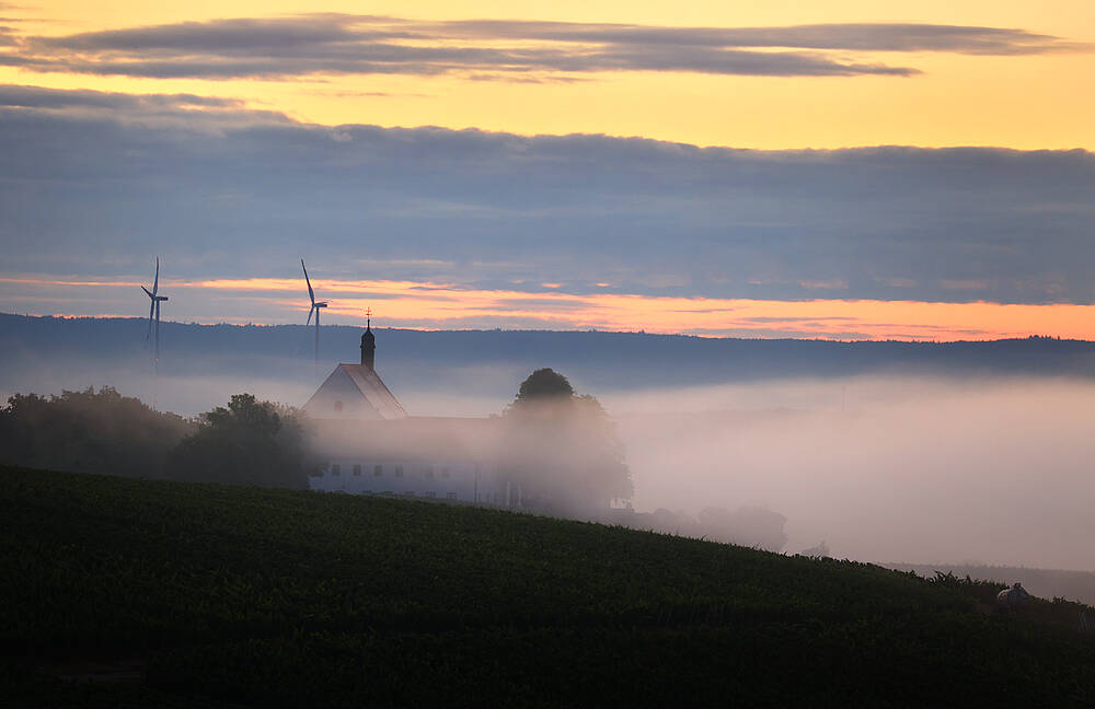 Zwei Windräder und eine Kirche verschwinden im Nebel (Symbolbild für Energiewende).