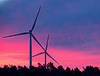 Windräder drehen sich in der Dämmerung vor einem blau-rosa gefärbten Himmel.