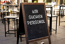 In einem Restaurant steht eine Tafel mit der Aufschrift "Wir suchen Personal".
