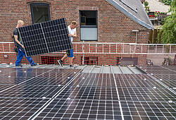 Zwei Handwerker installieren Photovoltaik-Module auf einem Hausdach.