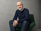 Porträtfoto des Astrophysikers Professor Harald Lesch sitzend auf einem Sessel.