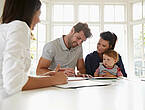 Ein junges Paar mit Kleinkind unterschreibt einen Vertrag, während eine Beraterin zusieht (Symbolfoto).