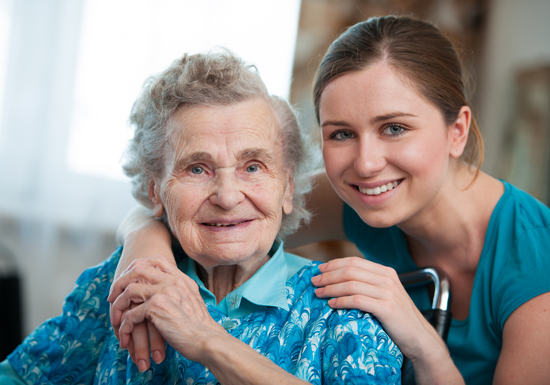 Symbolbild: Eine junge Pflegerin umarmt eine Seniorin.